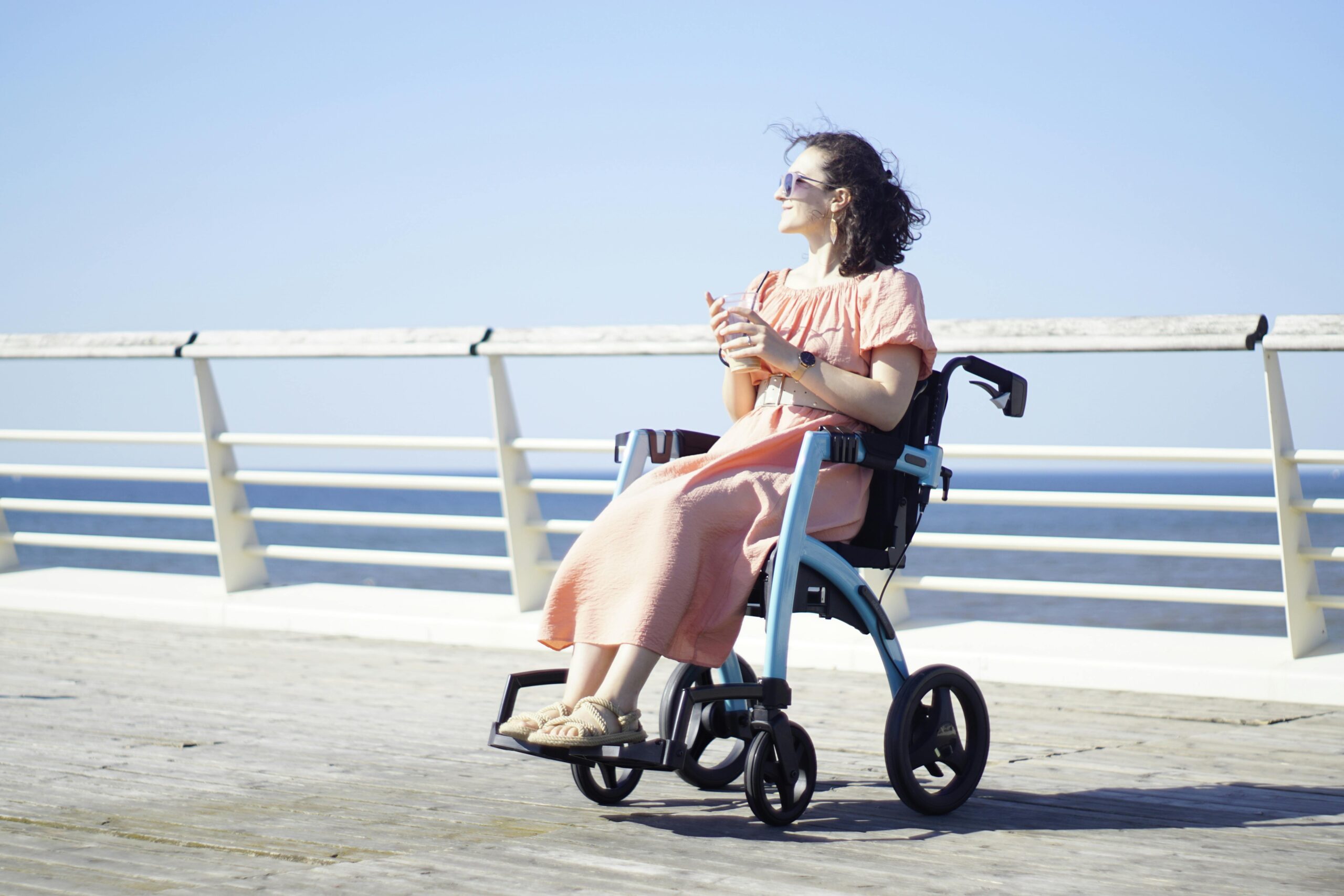 Woman in a transit wheelchair enjoying a sunny day on a pier, embodying freedom and mobility.